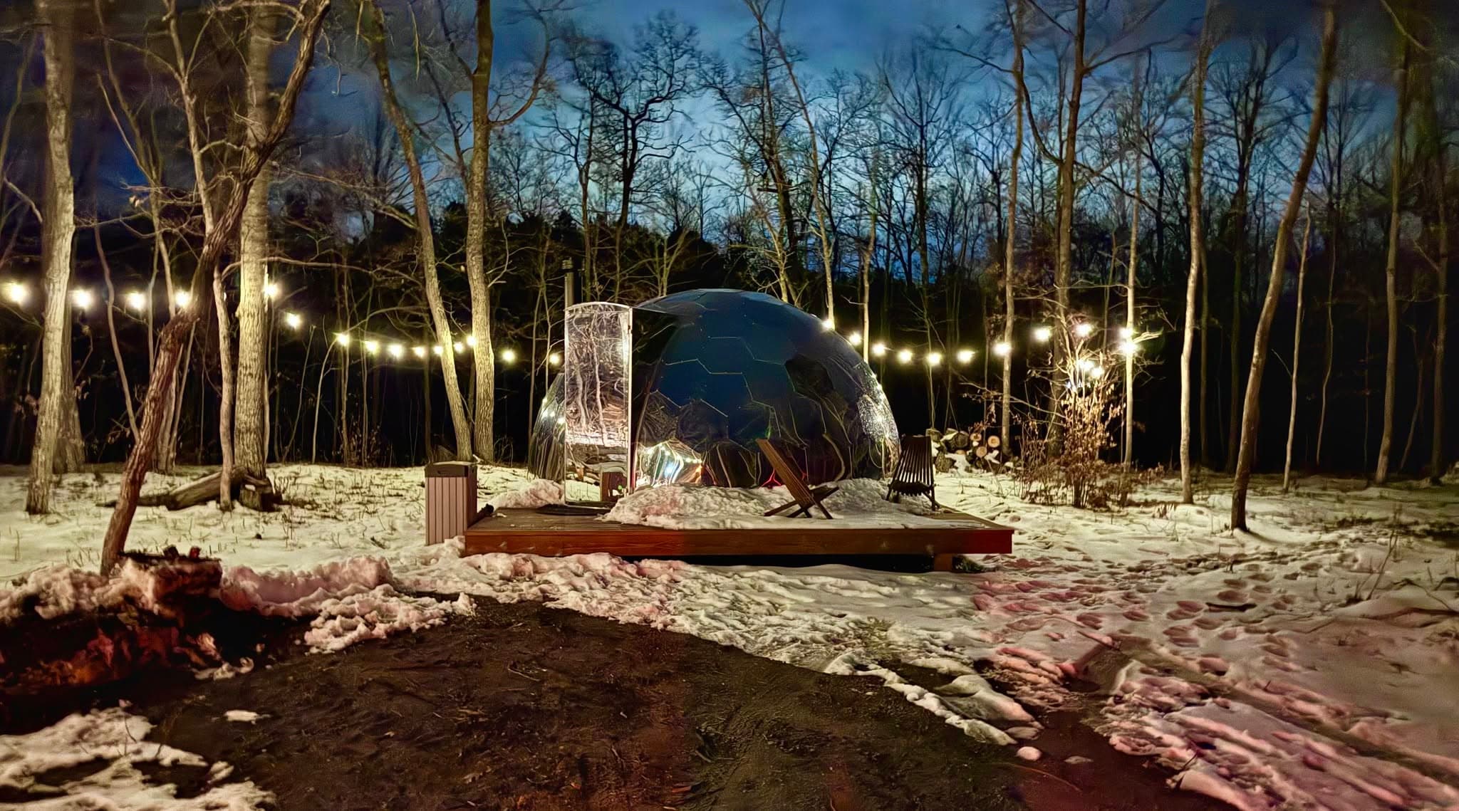 Dome lit by string lights at dusk with fire pit and Adirondack chairs